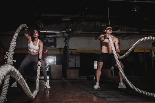 a man and woman whipping battle ropes in a CrossFit gym